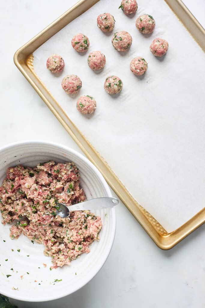 Meatballs being lined on a baking sheet