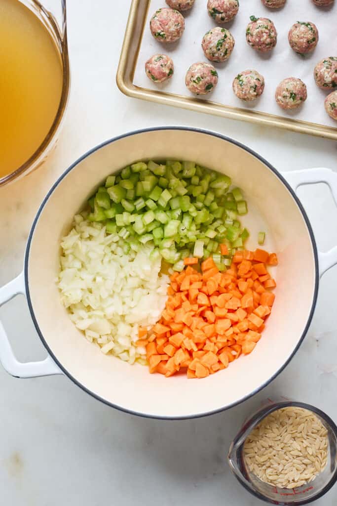 Carrots, onions and green peppers being added to a large dutch oven along with meatballs in the background