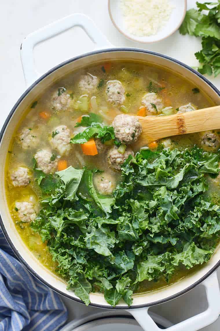 Kale being added to a large dutch oven filled with soup