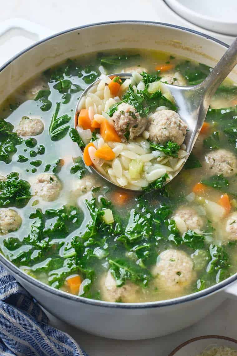 A large ladle lifting some Italian wedding soup out to serve