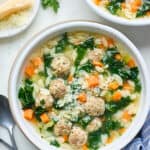 Bowls of Italian Wedding Soup against a white background with parmesan cheese in the background