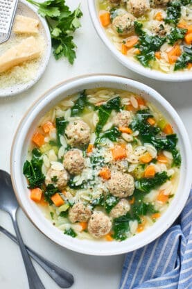 Bowls of Italian Wedding Soup against a white background with parmesan cheese in the background
