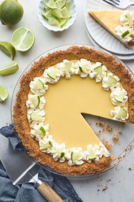 An overhead of a freshly baked key lime pie with a slice taken out on a white plate