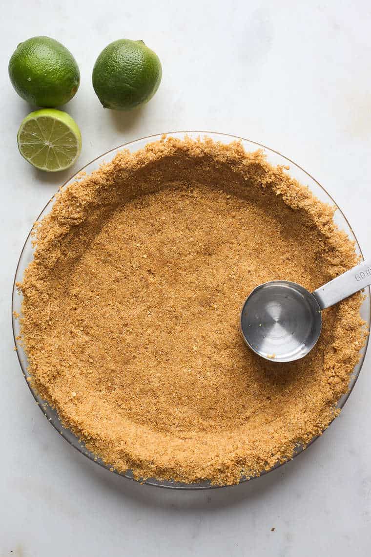 A graham cracker crust being pressed in with a measuring cup