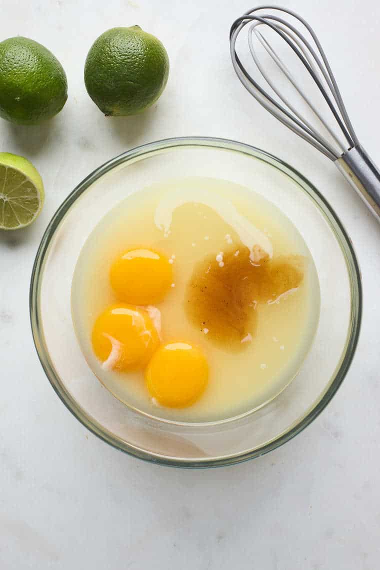 Egg yolks, milk, vanilla and key lime juice inside a clear bowl