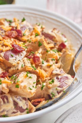 A close up of baked potato salad close up with a spoon sharing it