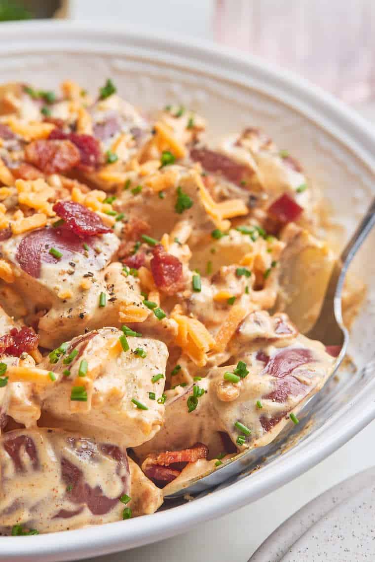 A close up of baked potato salad close up with a spoon sharing it