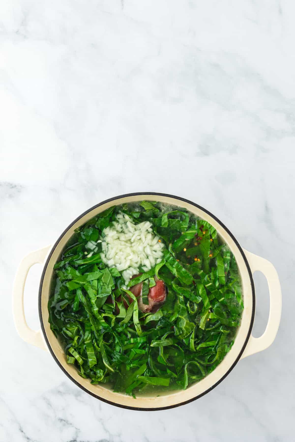 Mustard greens in a large white pot with seasonings and ingredients ready to cook down