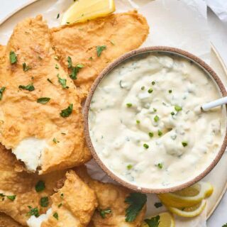 Pieces of fried fish on a white platter with a bowl of tartar sauce with a small spoon