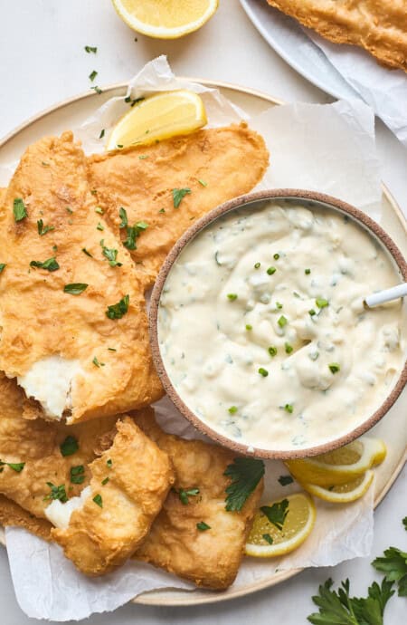 Pieces of fried fish on a white platter with a bowl of the best tartar sauce recipe with a small spoon