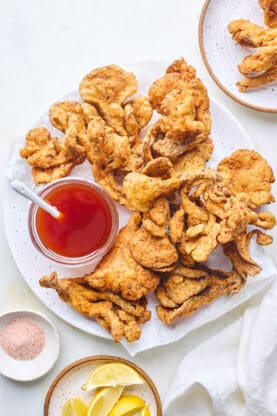 An overhead of vegan chicken fried oyster mushrooms on a white plate with spicy maple syrup