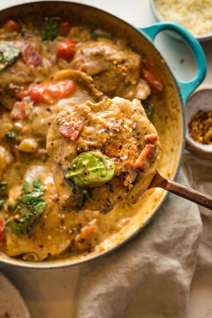 A close up of creamy garlic chicken skillet with a chicken thigh being lifted out