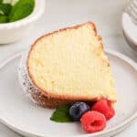 Slice of homemade pound cake with cream cheese on a white plate with berries.