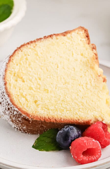 Slice of homemade pound cake with cream cheese on a white plate with berries.