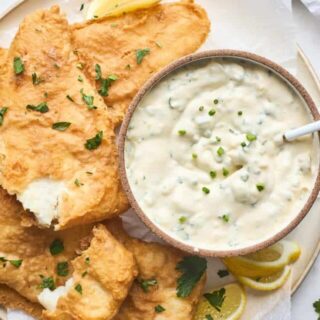 Pieces of fried fish on a white platter with a bowl of tartar sauce with a small spoon