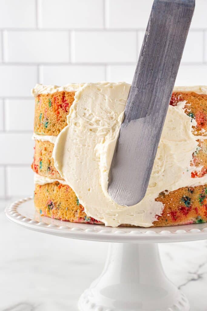 Vanilla buttercream being spread on sides of cake