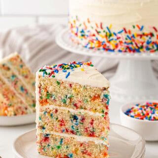 A slice of funfetti cake recipe on two white plates ready to enjoy with cake in background