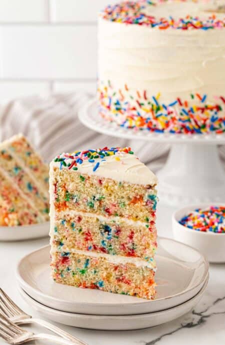 A slice of funfetti cake recipe on two white plates ready to enjoy with cake in background