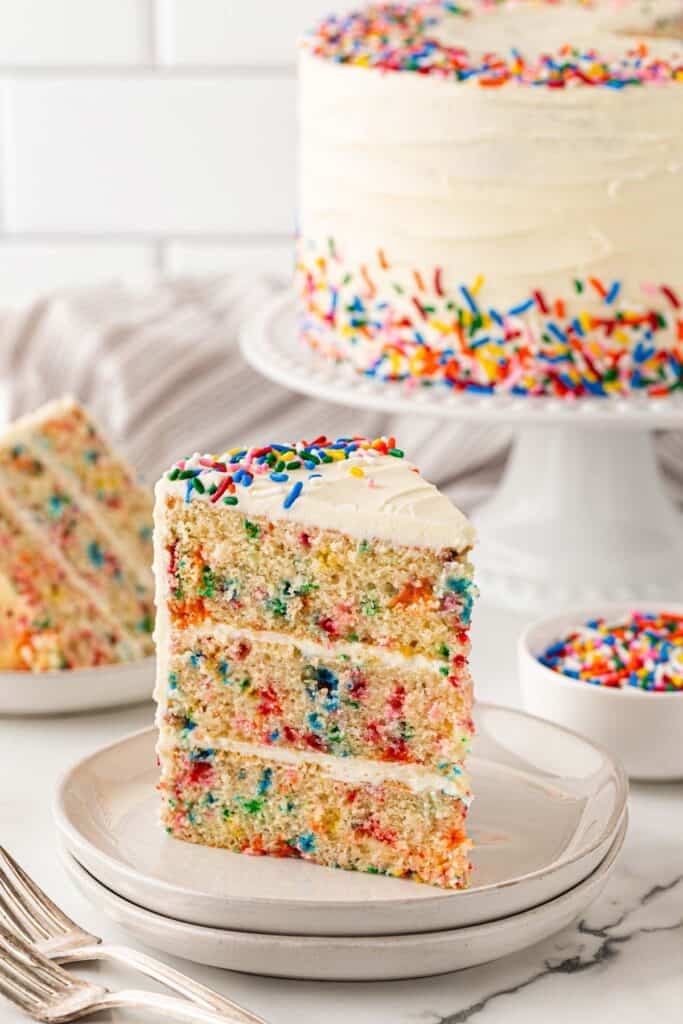 A slice of funfetti cake recipe on two white plates ready to enjoy with cake in background