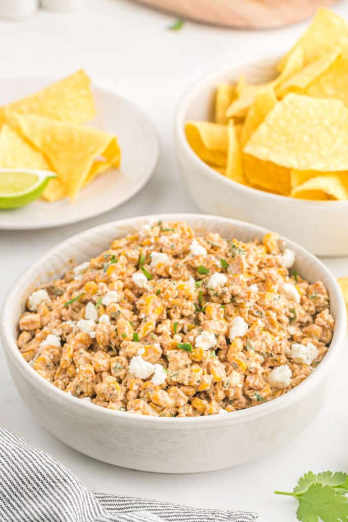A delicious Mexican corn elote dip recipe in a white bowl with tortilla chips in the white background ready to enjoy