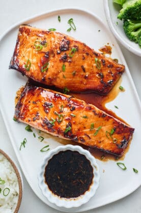 Two air fryer salmon filets on a white platter with honey garlic sauce in a bowl nearby