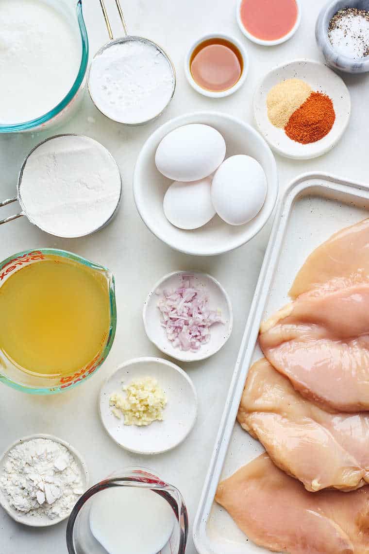 Ingredients for country fried steak: Chicken breasts, eggs, spices, and chicken stock against a white background