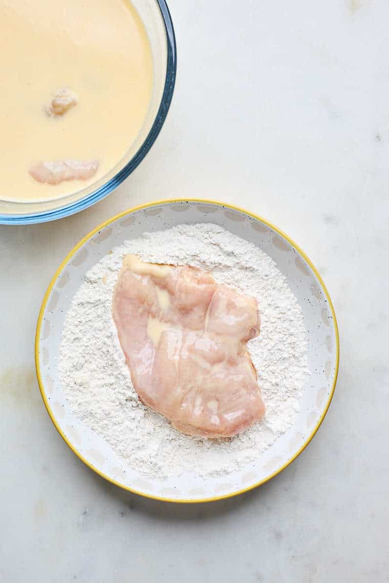 A chicken breast being floured in a seasoned flour mixture