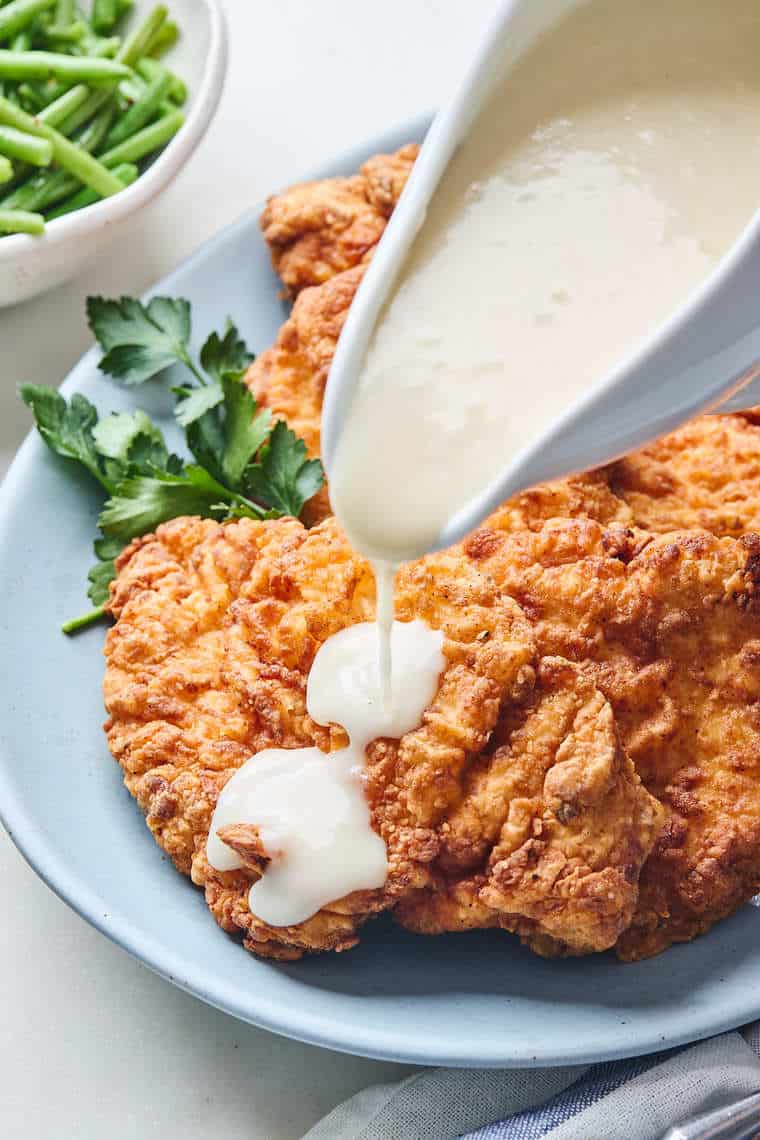 Chicken fried chicken on a blue plate with white gravy being poured over the top