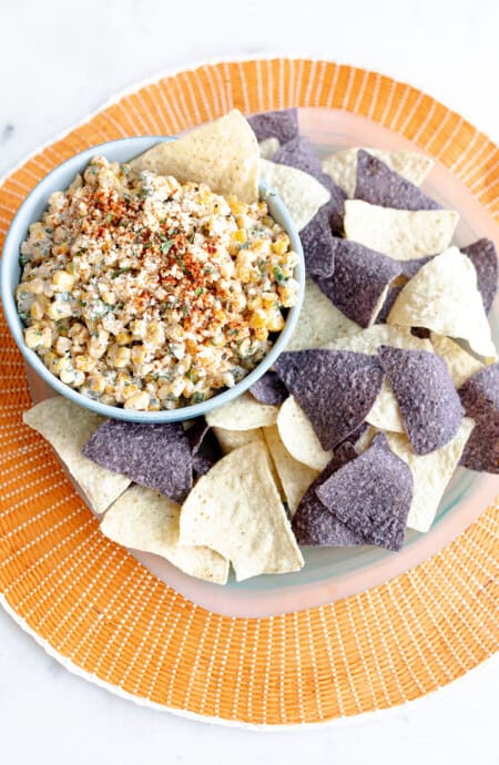 A beautiful orange plate with various tortilla chips and a bowl of elote dip recipe ready to serve
