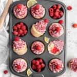 Raspberry lemon poke cupcakes in a cupcake pan with raspberries in some of the tins against a white background