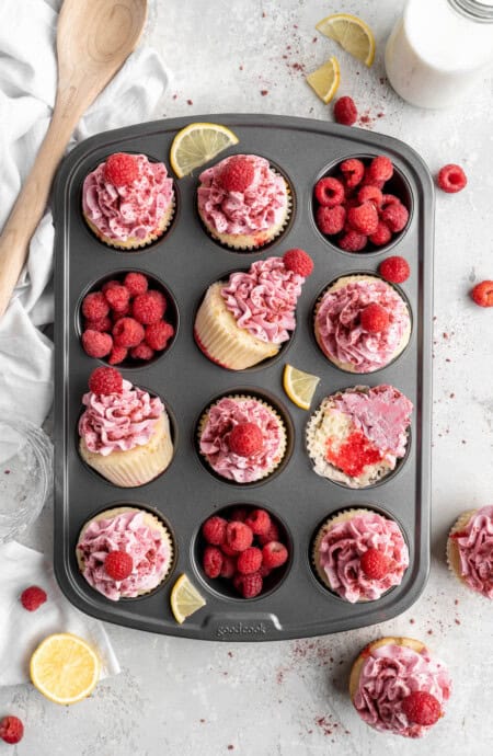 Raspberry lemon poke cupcakes in a cupcake pan with raspberries in some of the tins against a white background