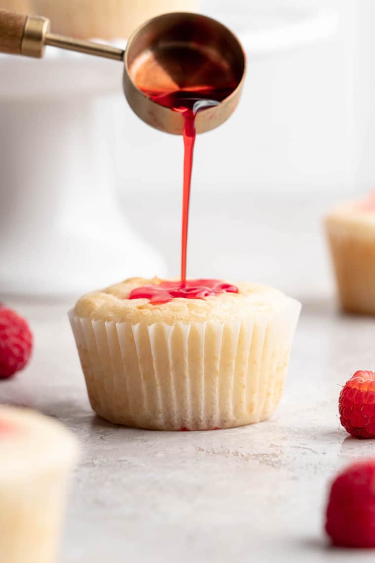 A close up of a lemon cupcake having raspberry syrup poured into the top of it