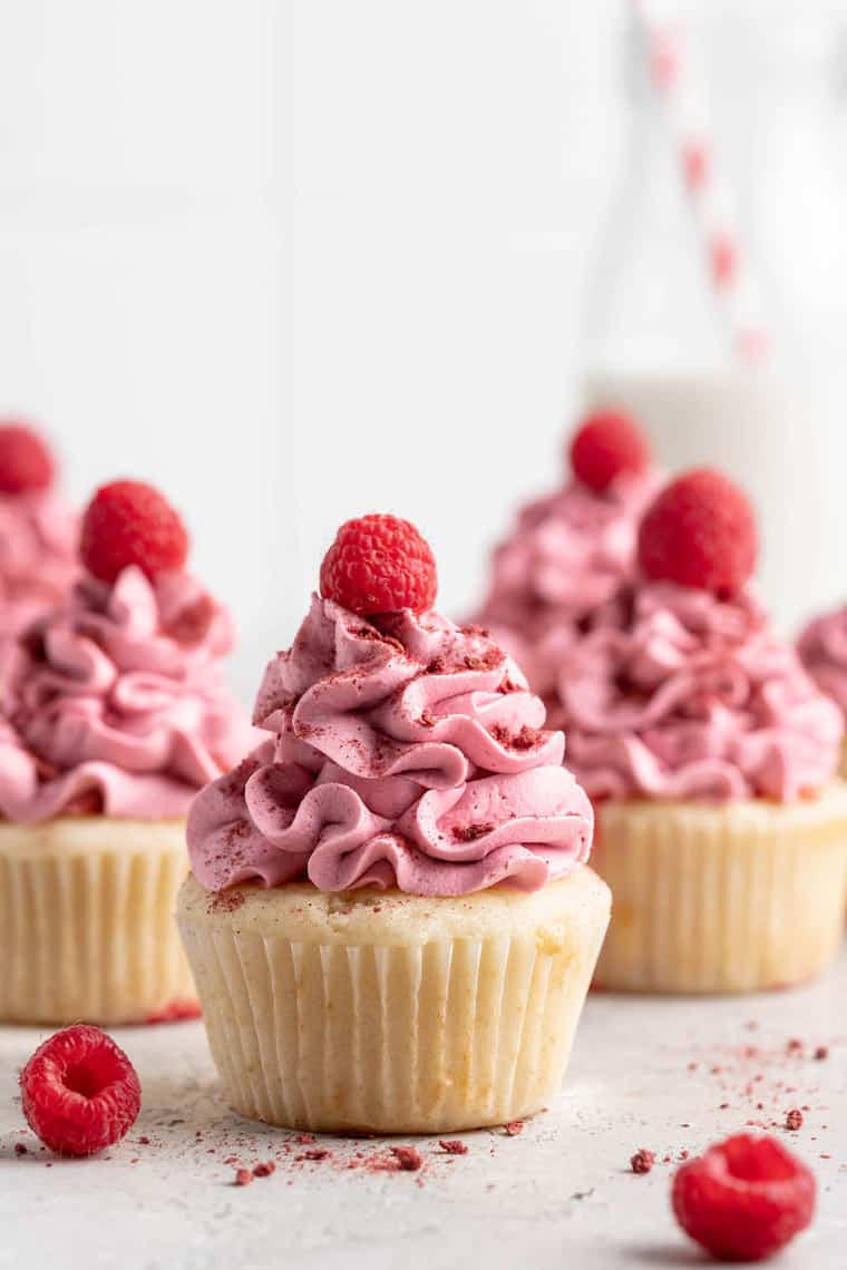 A close up of several raspberry lemon cupcakes with raspberry buttercream and raspberries on top against a white background