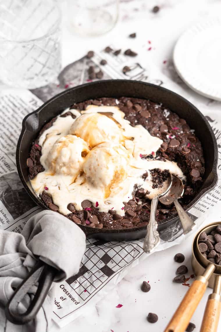 A skillet brownie baked in a cast iron with ice cream melting on top and two spoons