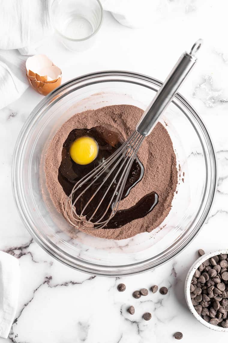 An egg being whisked into a dry cocoa powder mix