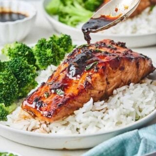 A honey garlic sauce being spooned over air fryer salmon on a plate with rice and broccoli