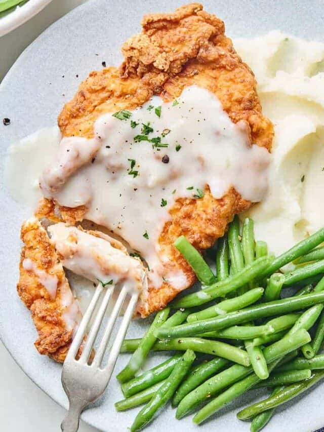 A close up of chicken fried chicken cut with a fork going into it to serve with mashed potatoes and green beans on a plate