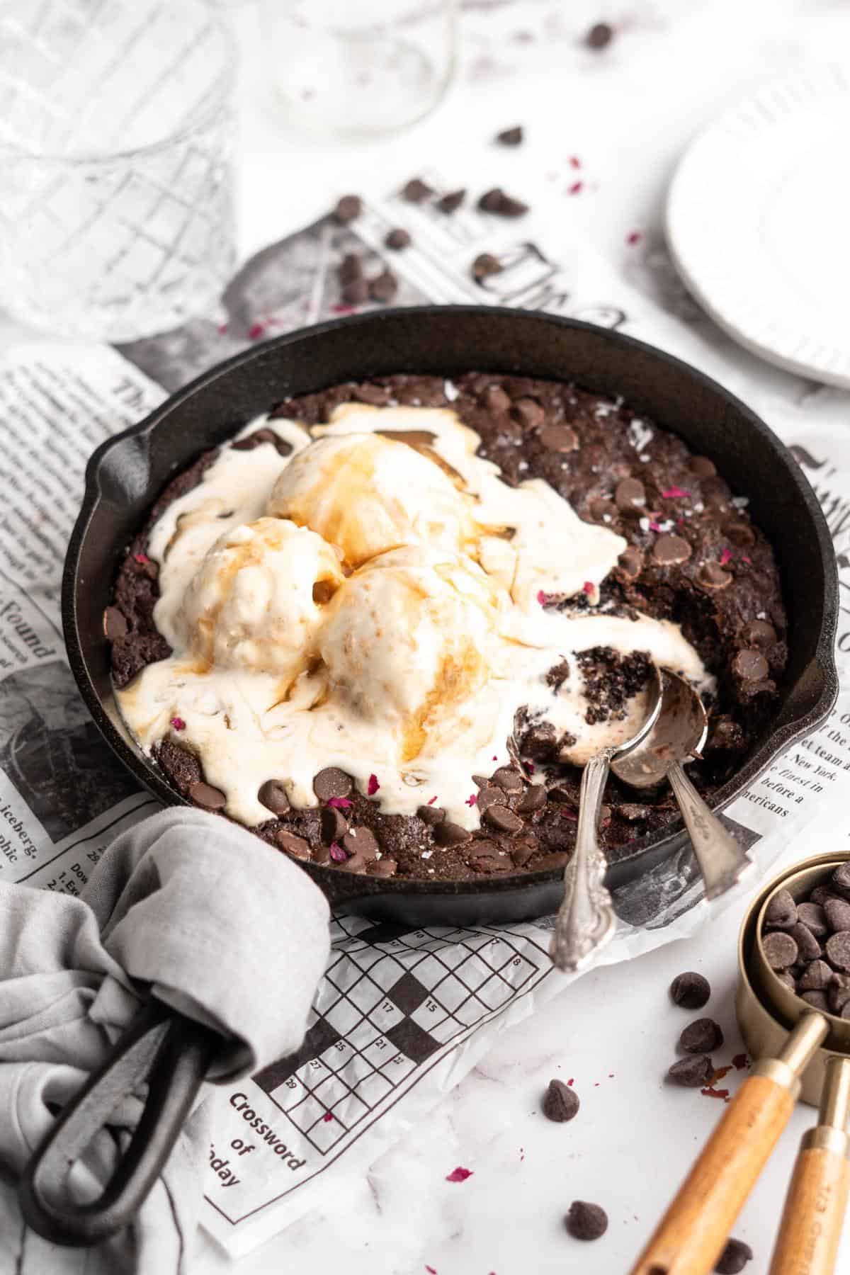 A skillet brownie baked in a cast iron with ice cream melting on top and two spoons