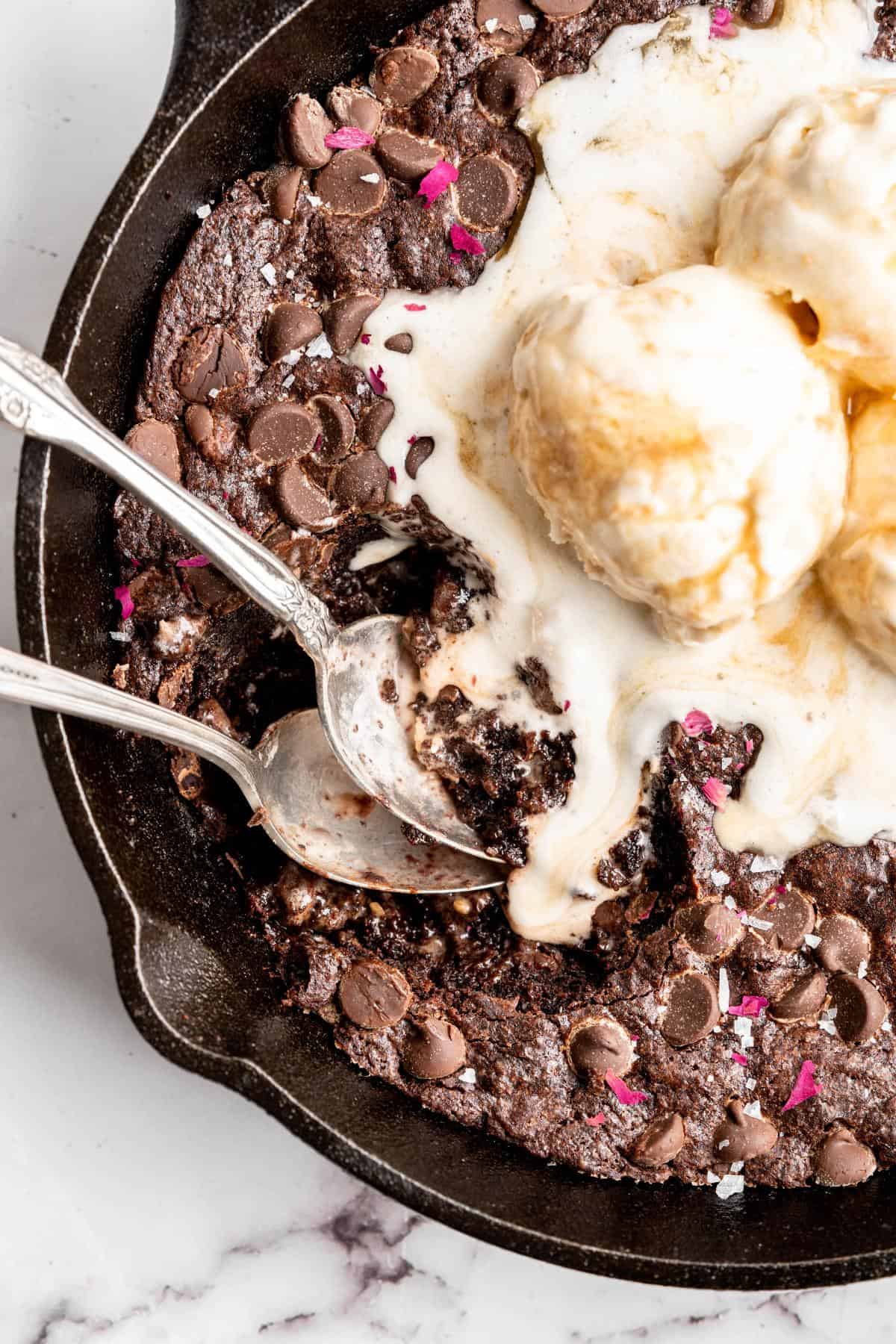 Closeup of a skillet brownie with three scoops of vanilla ice cream melting on top