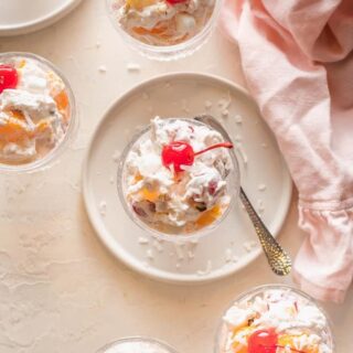 Southern ambrosia in small clear bowls with whipped cream and a cherry o top with a pink napkin