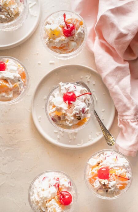 Southern ambrosia in small clear bowls with whipped cream and a cherry o top with a pink napkin