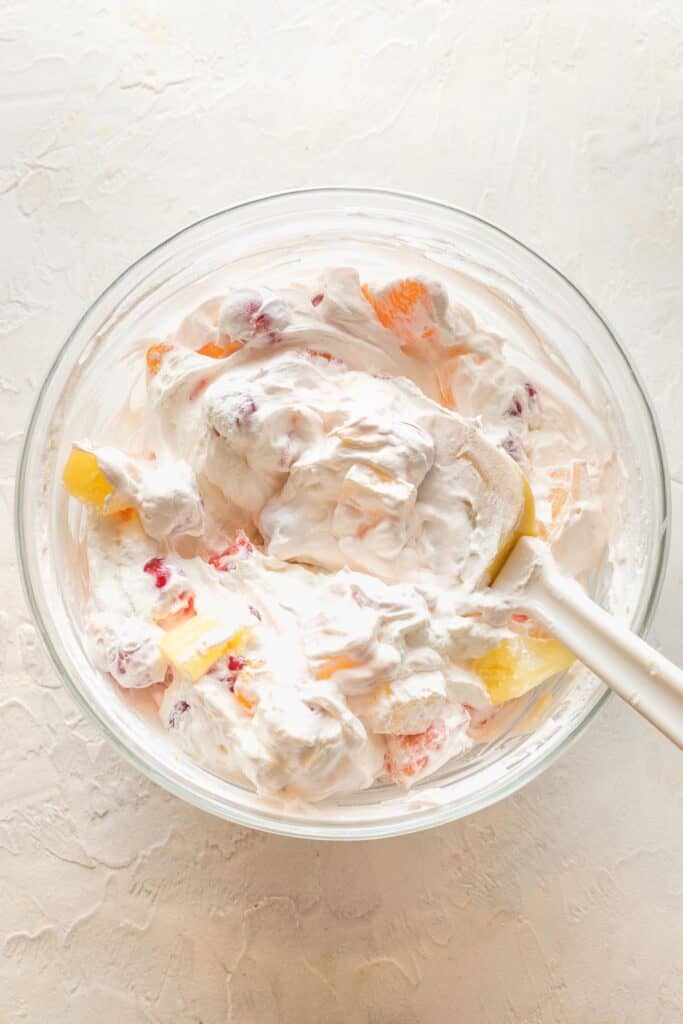 Ambrosia being folded together in a clear bowl with a spatula