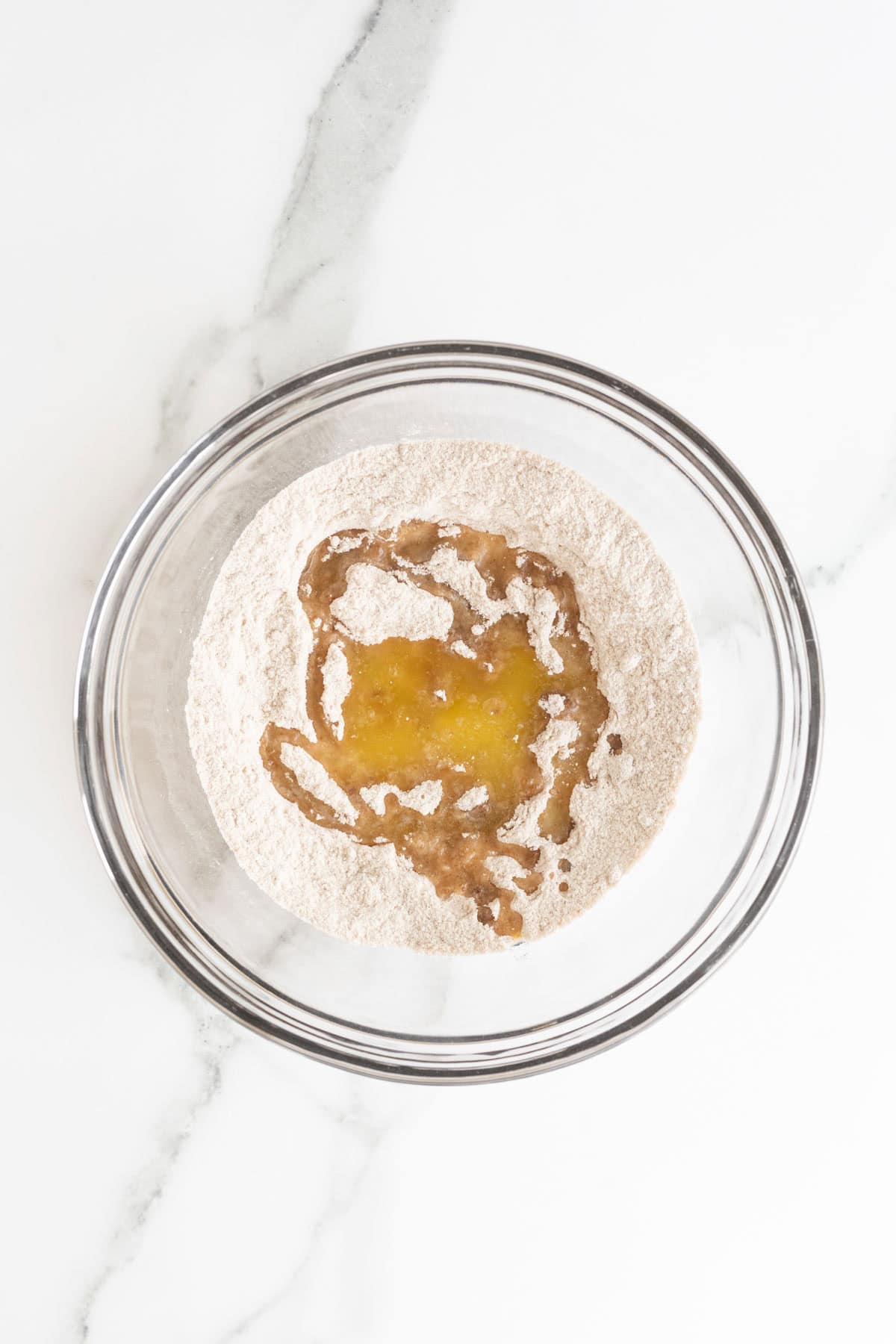 Overhead shot of a clear glass bowl with a light brown dry ingredient mixture, with melted butter poured into the center