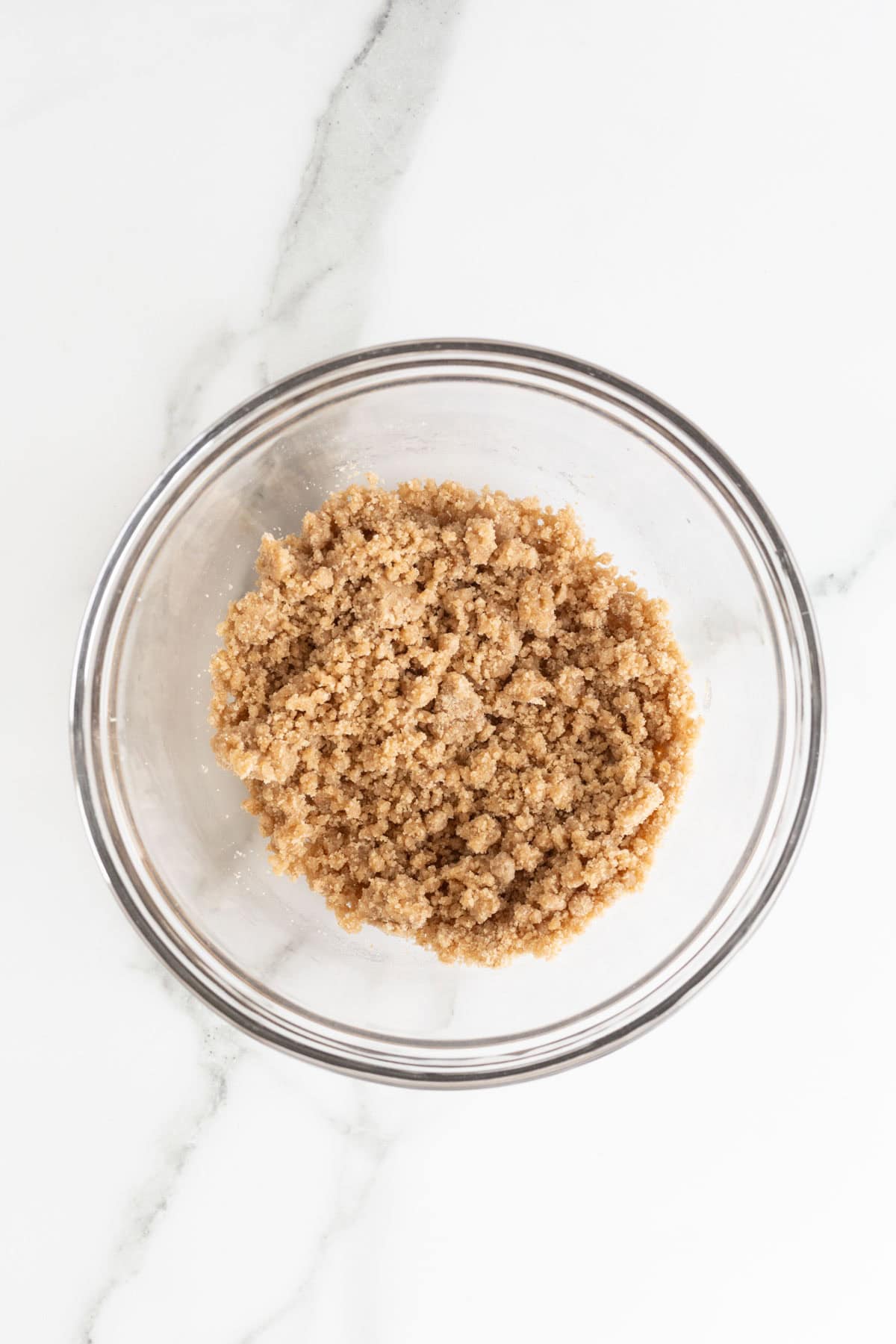 Overhead shot of a clear glass bowl filled with a golden-brown, crumble mixture