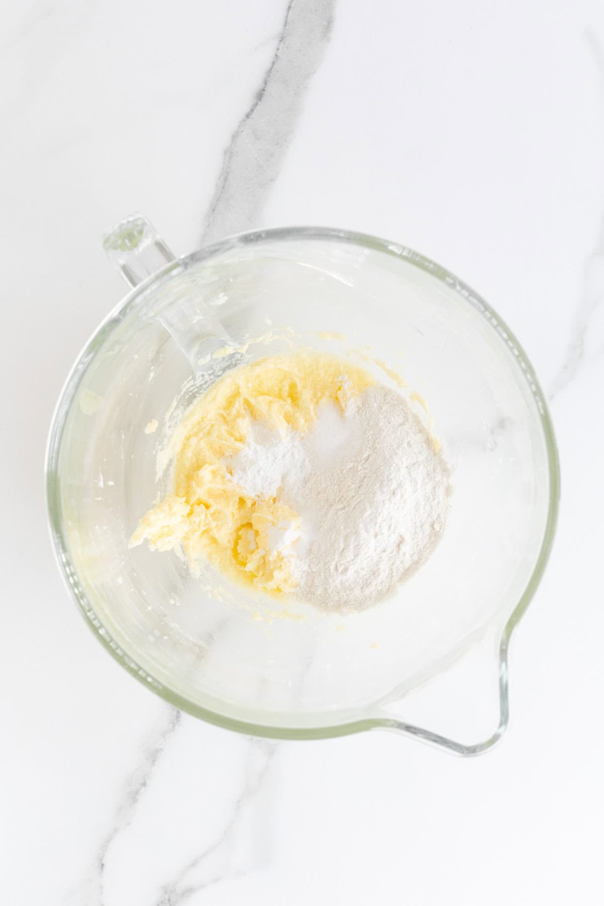 Overhead shot of a clear glass mixing bowl with softened butter and a pile of dry ingredients