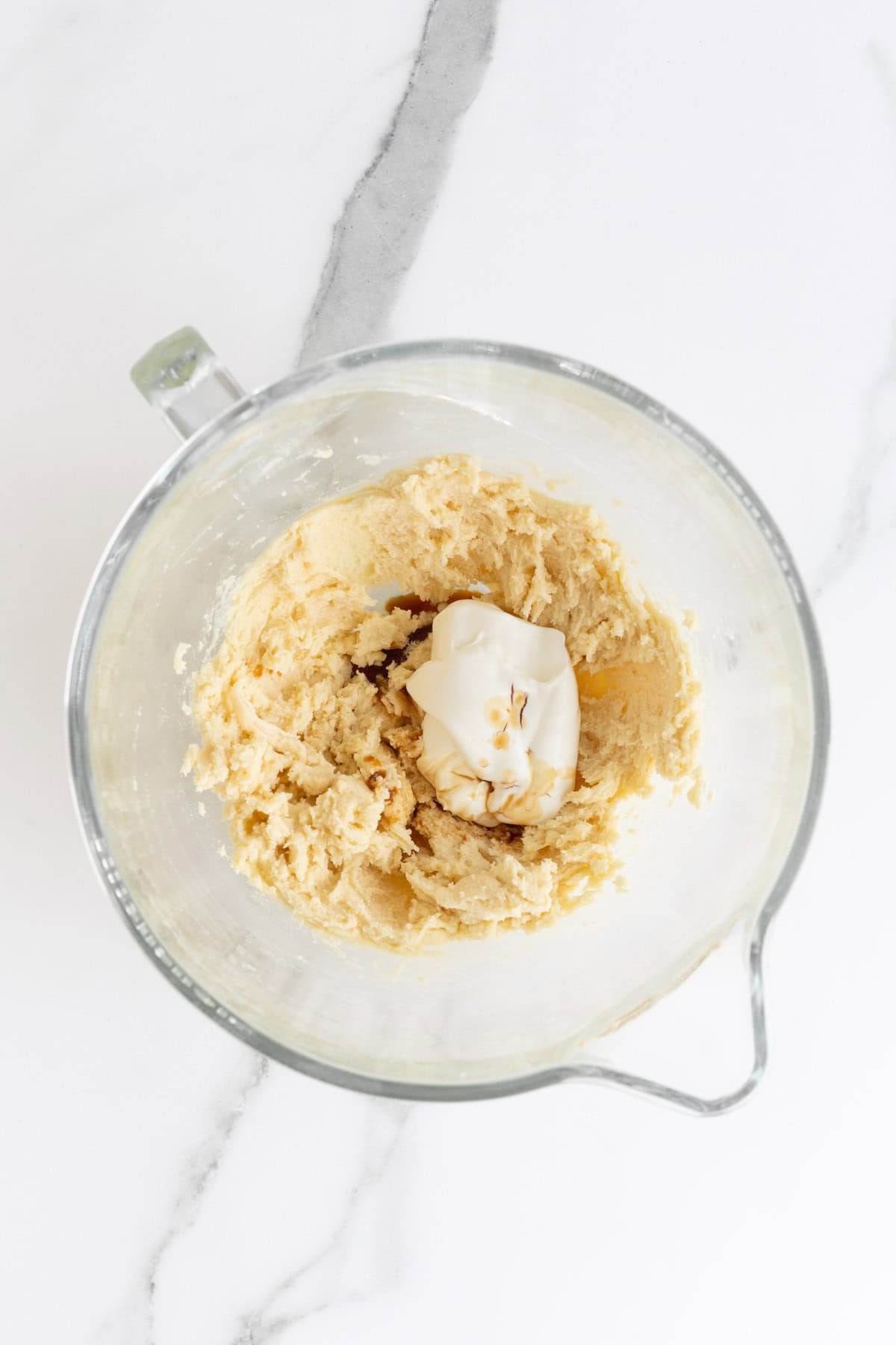 Overhead shot of a clear glass mixing bowl with a thick, light brown cake batter with sour cream and vanilla extract poured in