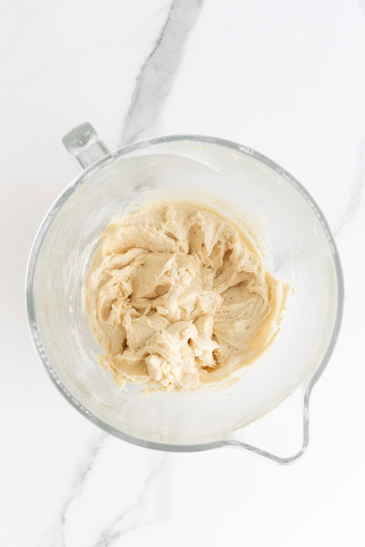 Overhead shot of a clear glass mixing bowl with a pale, creamy cake batter that has been fully mixed
