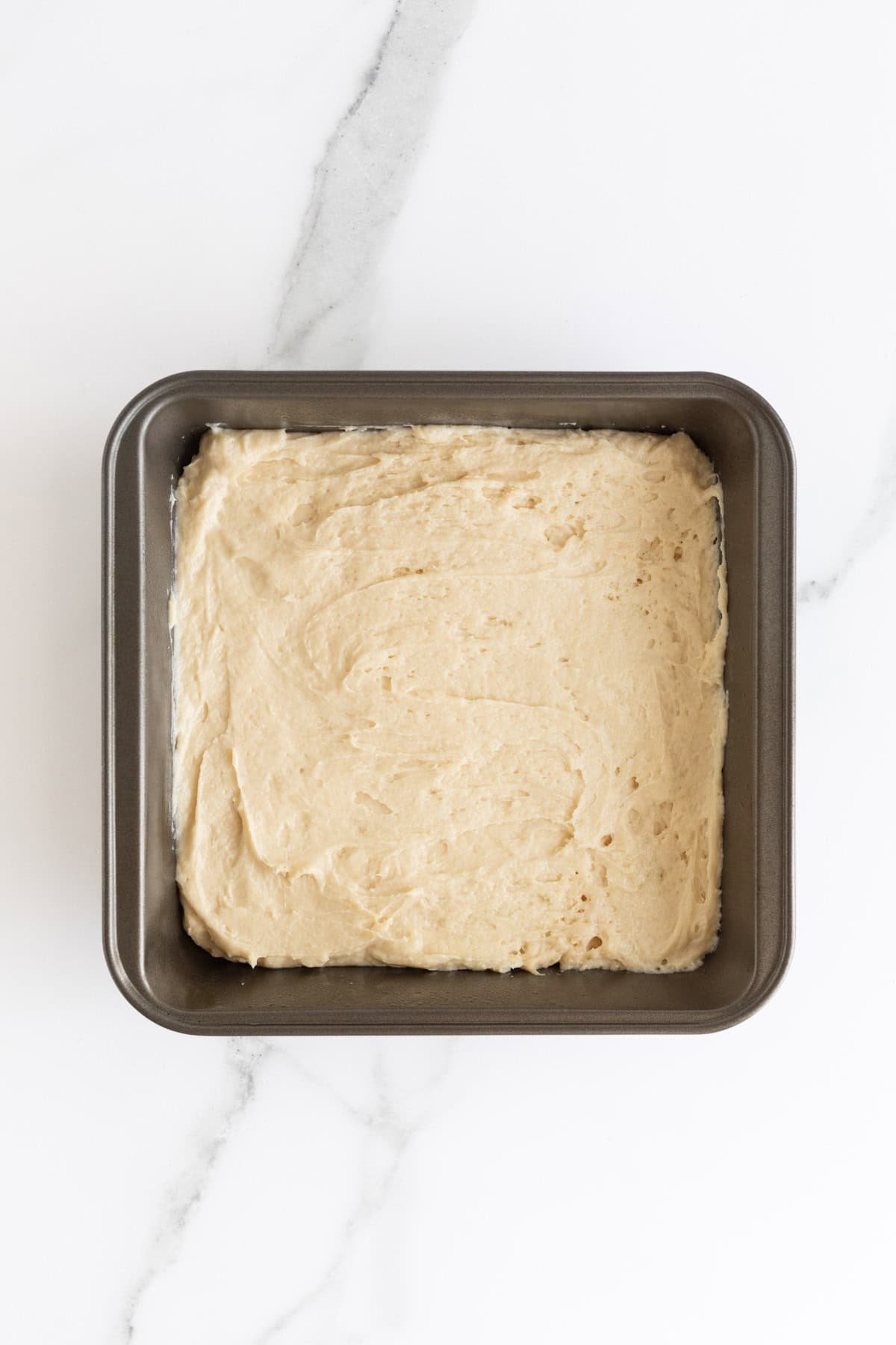 Overhead shot of a square baking pan filled evenly with a smooth, light-colored cake batter