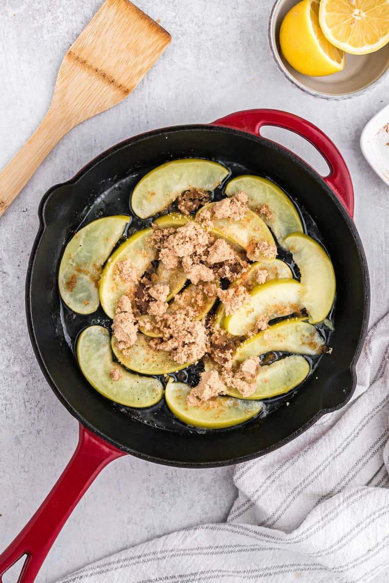 Sliced apples in a cast iron skillet with brown sugar sprinkled on top