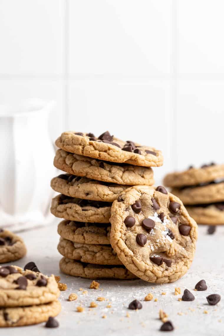 A stack of brown butter chocolate chip cookies with one leaning against it with a white background